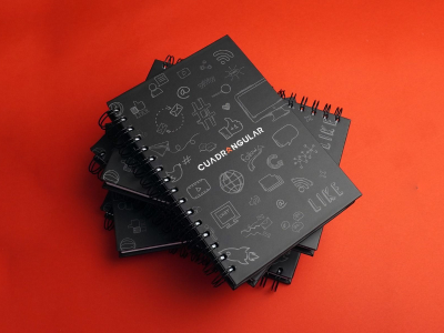 Stack of black spiral notebooks with CUADRANGULAR branding and white hand-drawn design icons on a vibrant red background
